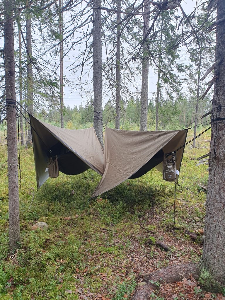 Kaksi tummanvihreää riippumattoa katoksineen vierekkäin syksyisessä metsässä.